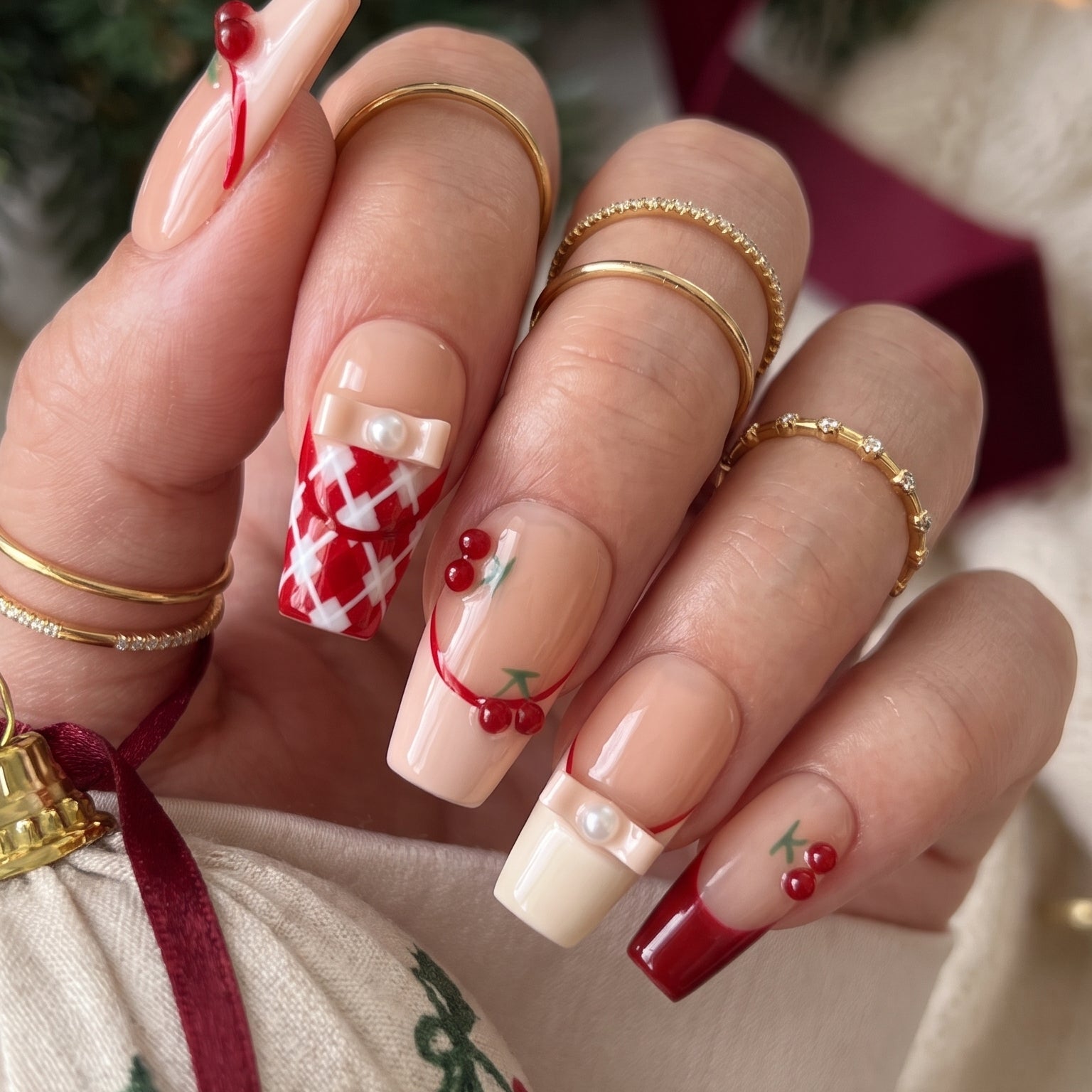 Cherry Ribbon Kiss red and nude pink press-on nails worn on hand, featuring long coffin nails with 3D cherries, pearl ribbon bows, plaid French tips, and sweet coquette nail art.