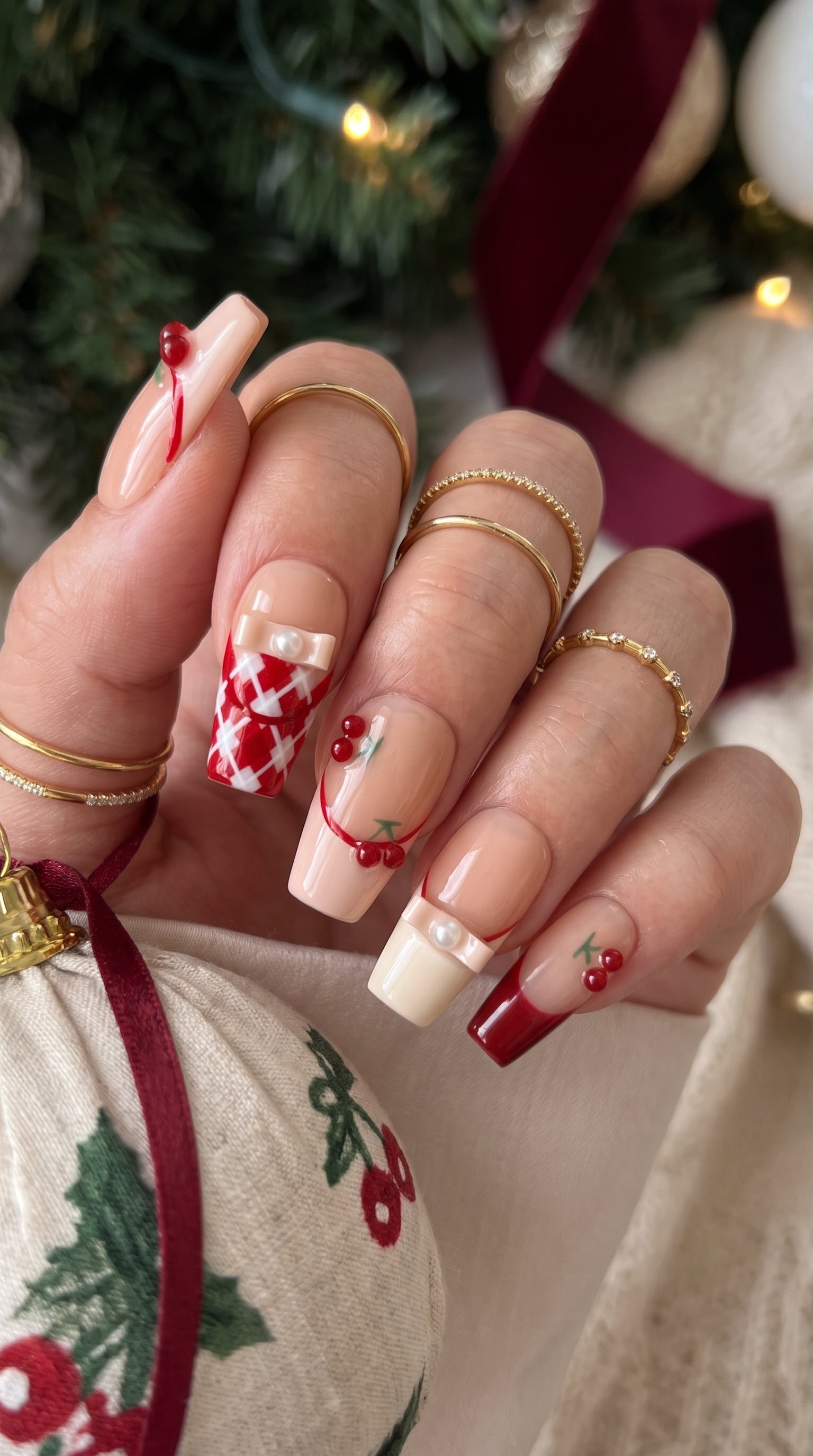 Cherry Ribbon Kiss red and nude pink press-on nails worn on hand, featuring long coffin nails with 3D cherries, pearl ribbon bows, plaid French tips, and sweet coquette nail art.