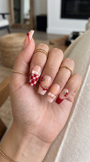 Cherry Ribbon Kiss red and nude pink press-on nails worn on hand, featuring long coffin nails with 3D cherries, pearl ribbon bows, plaid French tips, and sweet coquette nail art.