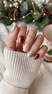Cocoa & Twinkle short oval Christmas press-on nails worn on hand, featuring chocolate brown chrome, cream white nails, red polka dots, a glittery Christmas tree, and sparkling silver confetti.