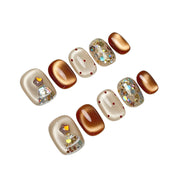 Cocoa & Twinkle short oval press-on nail set featuring metallic cocoa brown, creamy ivory, red polka dots, a sparkling Christmas tree design, and iridescent silver glitter accents.