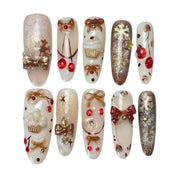 Gingerbread Wishes long almond press-on nail set featuring creamy ivory, champagne gold glitter, gingerbread-inspired nail art, 3D ribbon bows, red candy accents and sparkling stars.