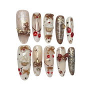 Gingerbread Wishes long almond press-on nail set featuring creamy ivory, champagne gold glitter, gingerbread-inspired nail art, 3D ribbon bows, red candy accents and sparkling stars.
