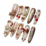 Gingerbread Wishes long almond press-on nail set featuring creamy ivory, champagne gold glitter, gingerbread-inspired nail art, 3D ribbon bows, red candy accents and sparkling stars.