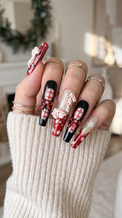 Midnight Candy Bows Christmas press-on nails worn on hand, featuring long coffin nails with red and black plaid designs, 3D candy canes, festive bows and sparkling snowflakes.